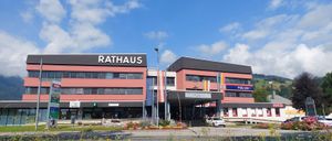Ein Rathaus mit 'Rathaus' oben, an einem sonnigen Tag gelegen, mit einem weißen Auto davor geparkt.