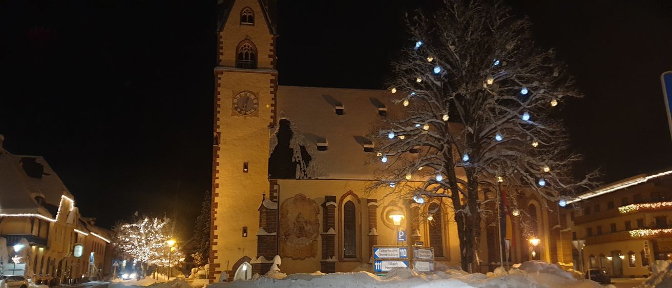 Eine Kirche mit Glockenturm und beschädigter Wand steht nachts im Schnee, beleuchtet von einer Straßenlampe.