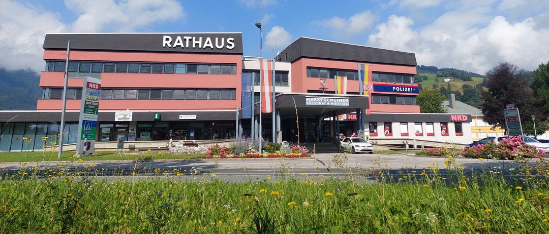 The Rathaus building in a small town, with a white car parked in front and a blue sky with clouds.