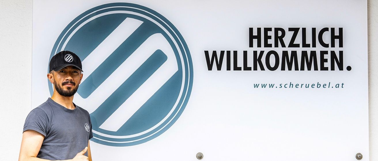 Ein blaues und weißes kreisförmiges Logo mit sich kreuzenden Streifen auf weißem Hintergrund. Die Wörter 'HE WILLKO' sind in schwarzer Schrift unter dem Logo geschrieben. Es gibt auch ein kleines Logo mit den Buchstaben 'WWW'.