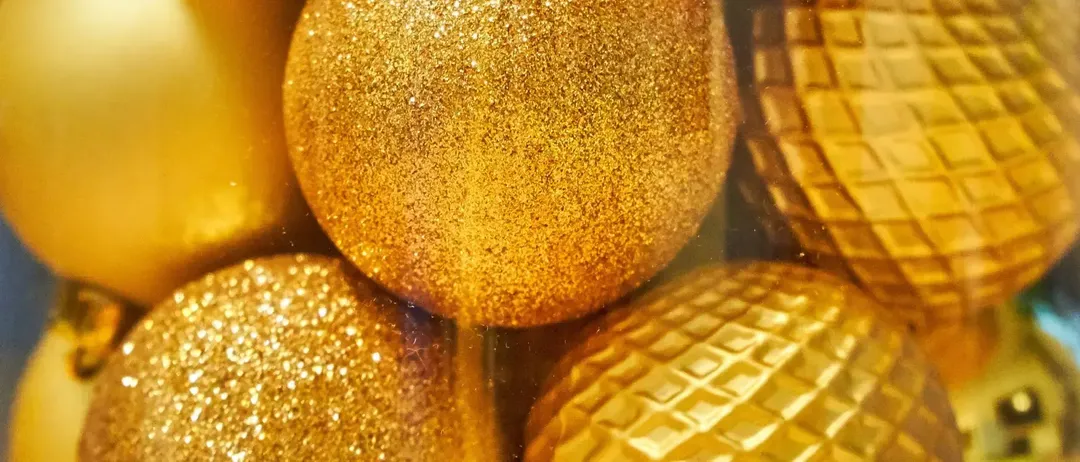 Eine Nahaufnahme verschiedener goldener Weihnachtskugeln, einige mit Glitzer und andere mit Diamantmustern, reflektieren Licht.