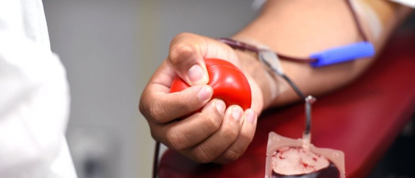 A person's hand squeezes a red ball to help draw blood into a bag connected to an IV.