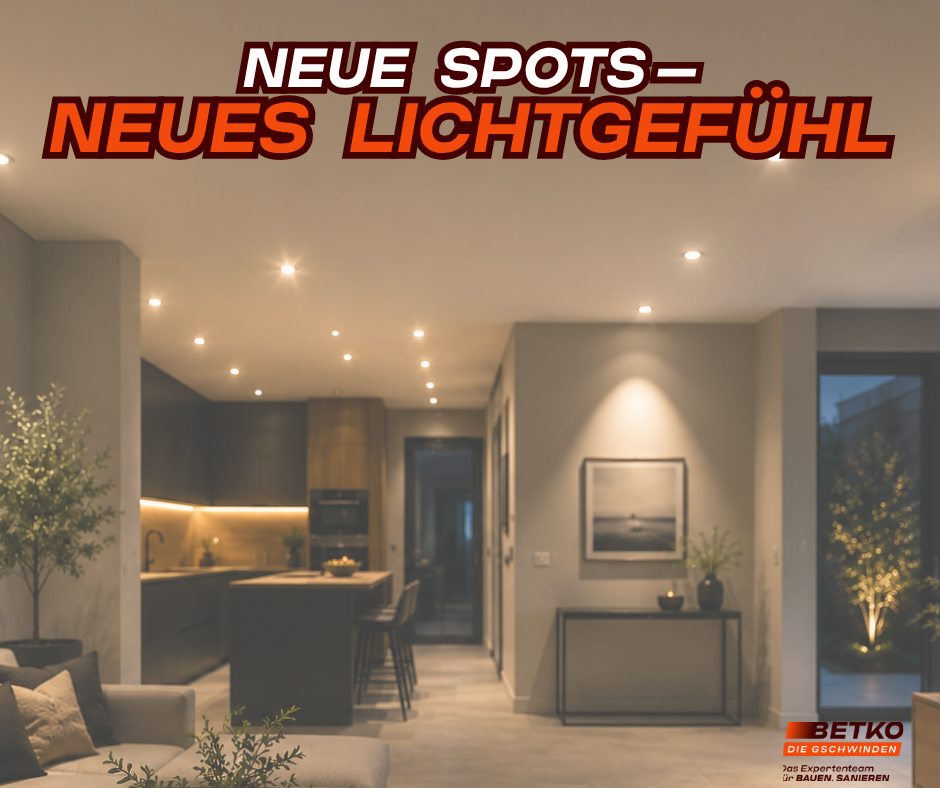 Ein Indoor-Foto von einer Küche und einem Wohnzimmer. Helle Beleuchtung ist an der Decke. Ein Sofa steht im Wohnzimmer.