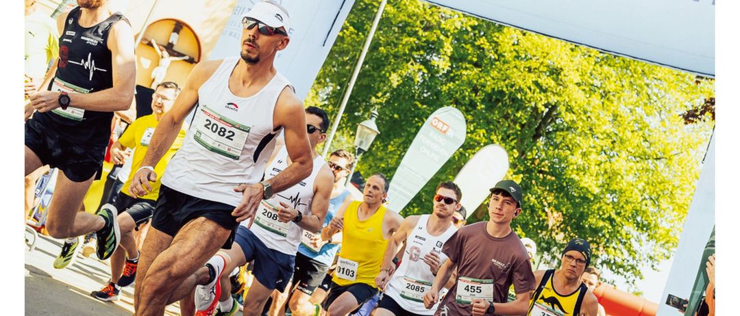 Läufer bei einem Marathon mit Nummern und Startnummern. Das Schild oben sagt 'Bad Waltersdorf'. Der Text unten sagt 'Radio Steiermark Lauf Jetzt anmelden'.