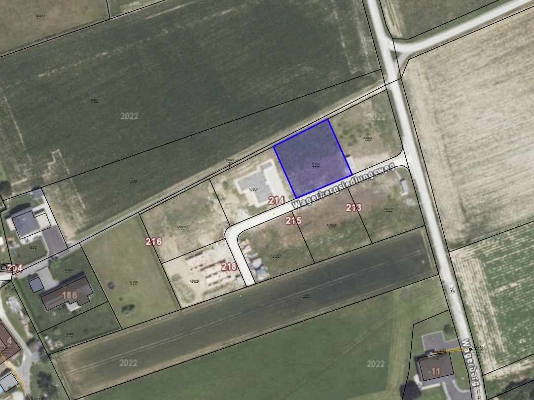 An aerial view of a property with a blue-shaded area marked as 214. It is surrounded by other numbered plots. Roads and paths are visible, with one labeled 'Wagenstraat'. The surrounding area is mostly green with some dirt patches.