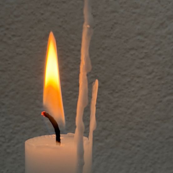 Eine Nahaufnahme einer brennenden Kerze mit einer hellen gelben Flamme vor einem grauen Hintergrund.