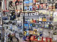 Eine Wand voller verschiedener Fahrradteile und Zubehör, auf Haken und Regalen organisiert, mit farbenfrohen Verpackungen und Etiketten.