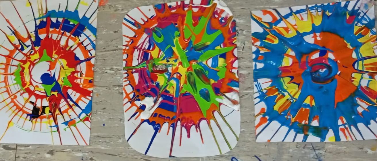 Ein abstraktes Kunstwerk mit leuchtenden Farben, das eine Kombination aus blauen, grünen, orangefarbenen und roten Spritzern auf einer weißen Oberfläche zeigt.