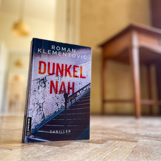Ein Buch mit dem Titel 'Dunkel Nah' von Roman Klementov liegt auf einem Holzboden. Das Buchcover zeigt eine Treppenabbildung.