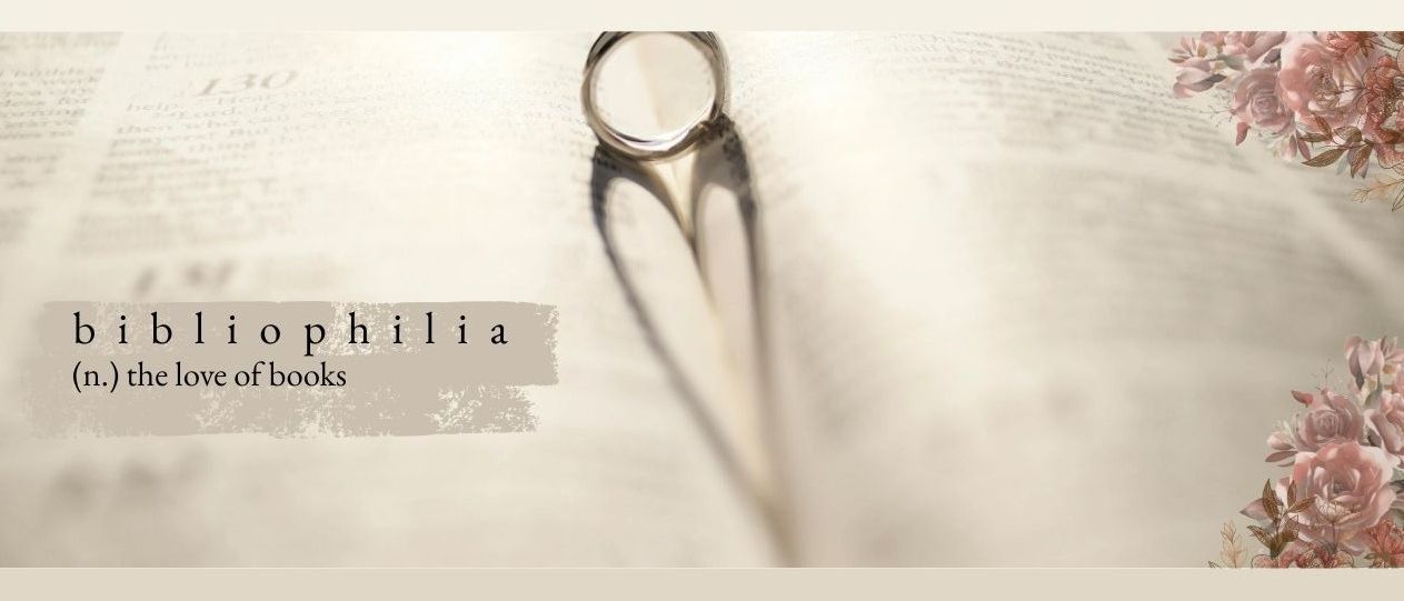 Ein silberner Ring liegt auf einem offenen Buch mit dem Titel 'Ophilia Books'. Der Schatten des Rings bildet ein Herz auf der Seite. Das Bild ist weich fokussiert und betont den Ring und seinen Schatten.