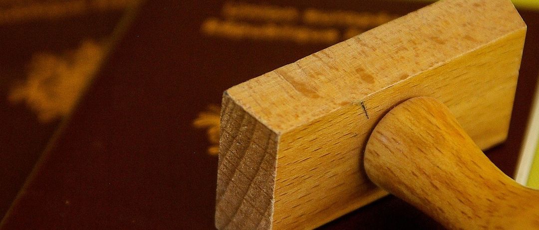 Ein hölzerner Stempel liegt auf einem Reisepass, der auf einem weiteren Reisepass auf einer grünen Oberfläche liegt.