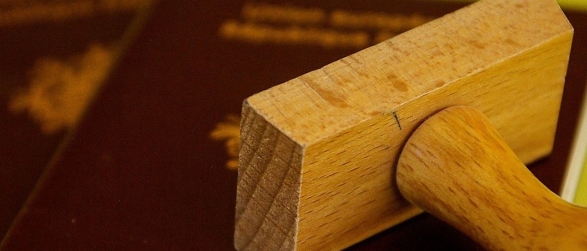 Ein hölzerner Stempel liegt auf einem Reisepass, der auf einem weiteren Reisepass auf einer grünen Oberfläche liegt.