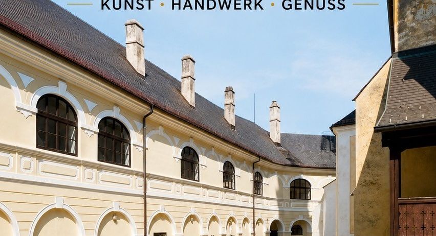 Ein Bild eines historischen Gebäudes mit einem Innenhof, mit einem Schild, das 'Hereinspaziert!' in einer dekorativen Schrift zeigt und Besucher einlädt, ein Wochenende wie bei Freunden zu erleben. Das Gebäude hat mehrere bogenförmige Fenster und Türen, mit einem Kopfsteinpflasterweg, der zum Eingang führt. Das Bild enthält auch die Daten 'Samstag, 8. August' und 'Sonntag, 9. August'.