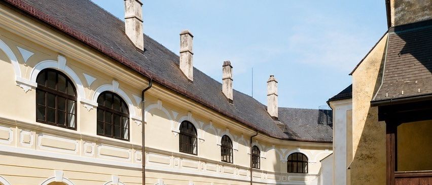 Ein Bild eines historischen Gebäudes mit einem Innenhof, mit einem Schild, das 'Hereinspaziert!' in einer dekorativen Schrift zeigt und Besucher einlädt, ein Wochenende wie bei Freunden zu erleben. Das Gebäude hat mehrere bogenförmige Fenster und Türen, mit einem Kopfsteinpflasterweg, der zum Eingang führt. Das Bild enthält auch die Daten 'Samstag, 8. August' und 'Sonntag, 9. August'.