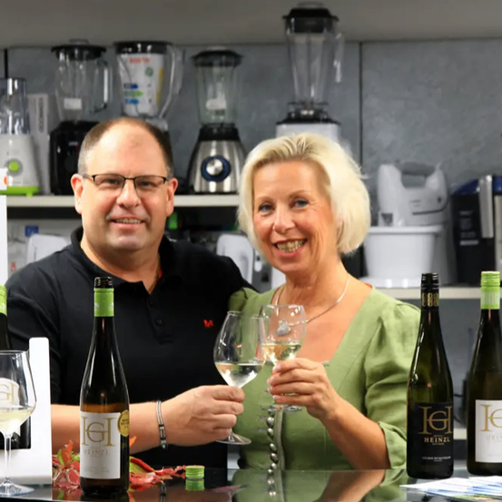 Ein Mann und eine Frau posieren für ein Foto mit Weingläsern und Flaschen in einer Küche.