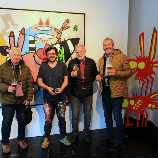 Vier Männer stehen vor einer Wand mit einem Gemälde. Jeder Mann hält ein Glas Wein. Die Wand ist mit abstrakten Gemälden verziert.