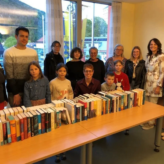 Eine Gruppe von Menschen steht und sitzt um einen mit Büchern gefüllten Tisch, wahrscheinlich in einer Bibliothek. Sie lächeln und posieren für ein Foto.