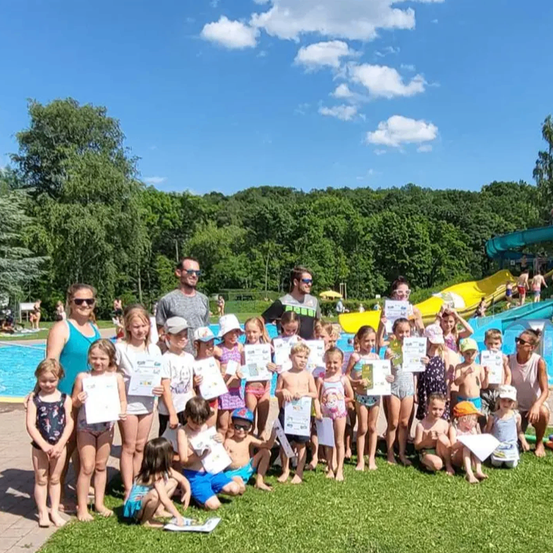 Eine Gruppe von Kindern und Erwachsenen posiert für ein Foto in einem Wasserpark mit Rutschen und Pools im Hintergrund.