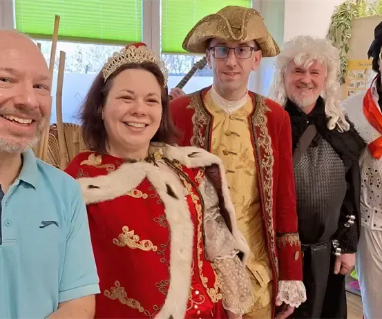 Fünf Menschen in Kostümen posieren für ein Foto, darunter eine Frau in einem roten Kleid, ein Mann in einem Piratenhut und ein anderer im Elvis-Outfit.