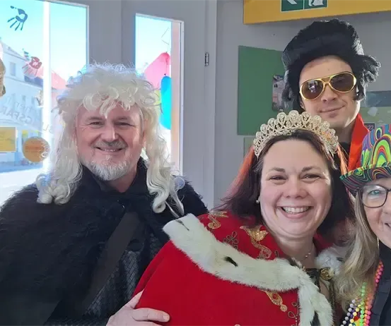 Fünf Personen in Kostümen und Hüten posieren für ein Foto in einem Raum mit Glasfenstern.