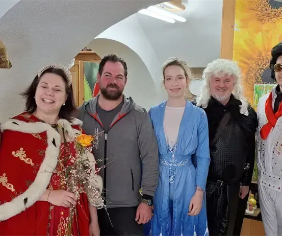 Eine Gruppe von Menschen in verschiedenen Kostümen, darunter ein König, eine Königin und Elvis, stehen zusammen und lächeln für ein Foto.