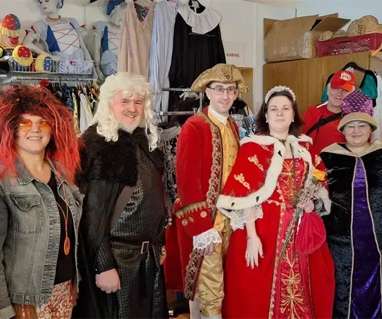 Eine Gruppe von Menschen in Kostümen posiert für ein Foto in einem Geschäft. Eine Frau in einem roten Kleid hält Blumen.