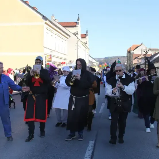 Eine Gruppe von Musikern in Kostümen, darunter Mönche, Zauberer und Clowns, marschiert mit Trompeten, Flöten und anderen Instrumenten bei einem Umzug.