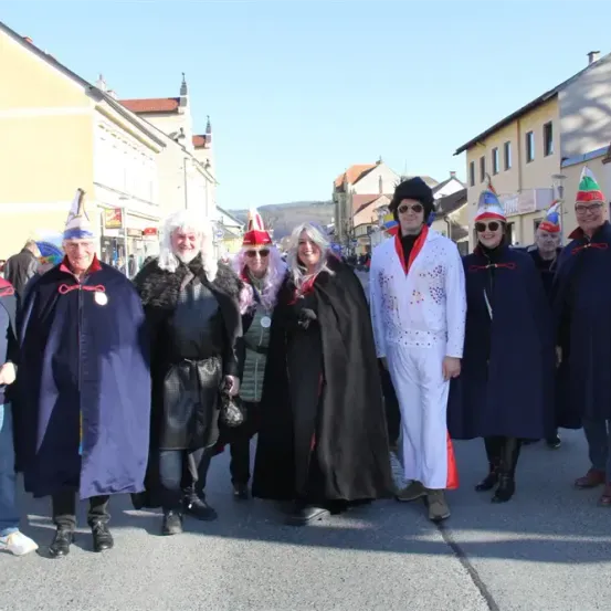 Eine Gruppe von Menschen in verschiedenen Kostümen, darunter ein weißer Elvis-Anzug, steht in einer Reihe auf der Straße.