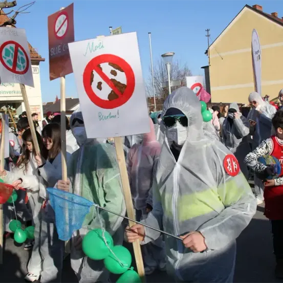 Eine Gruppe von Menschen in Schutzanzügen und mit Schildern demonstriert, einer hält ein Netz und grüne Luftballons.