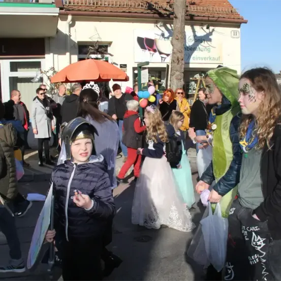 Eine Straße voller Menschen in Kostümen, mit Luftballons und Gesichtsbemalung. Ein Kind mit einem Schwert und ein Mädchen mit grüner Gesichtsbemalung sind im Vordergrund.