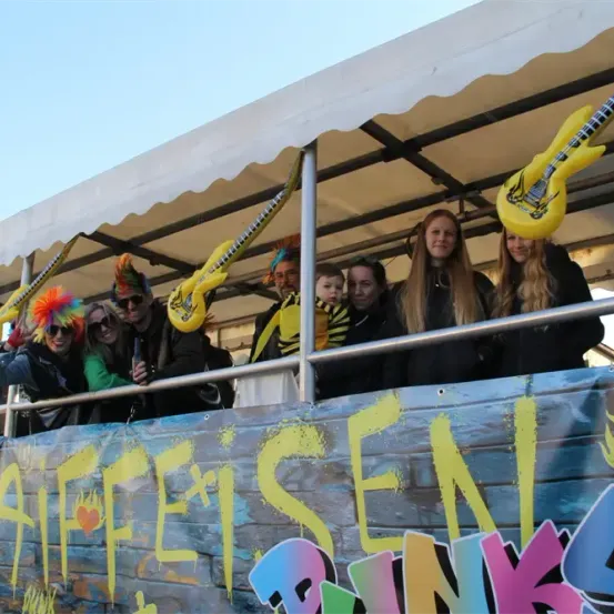 Eine Gruppe von Menschen in Kostümen steht auf einem Paradewagen mit Graffiti, hält Gitarren und posiert für ein Foto.