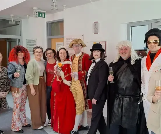 Eine Gruppe von Menschen in Kostümen, wahrscheinlich für eine thematische Veranstaltung, stehen zusammen und lächeln, während sie Weingläser halten.