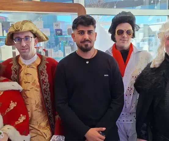 Fünf Personen in verschiedenen Kostümen, darunter ein Pirat, ein König, Elvis und zwei weitere, posieren für ein Foto in einem Geschäft.