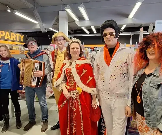 Eine Gruppe von Menschen in Kostümen, die für ein Foto in einem Geschäft mit einem Partyschild im Hintergrund posieren.