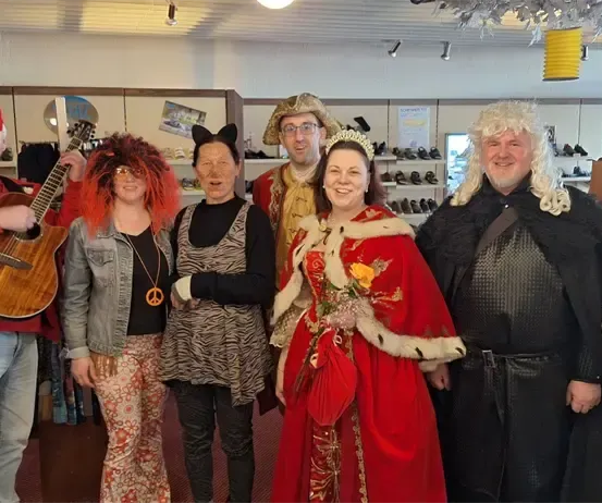 Eine Gruppe von Menschen in verschiedenen Kostümen steht in einem Raum und posiert lächelnd für ein Foto.