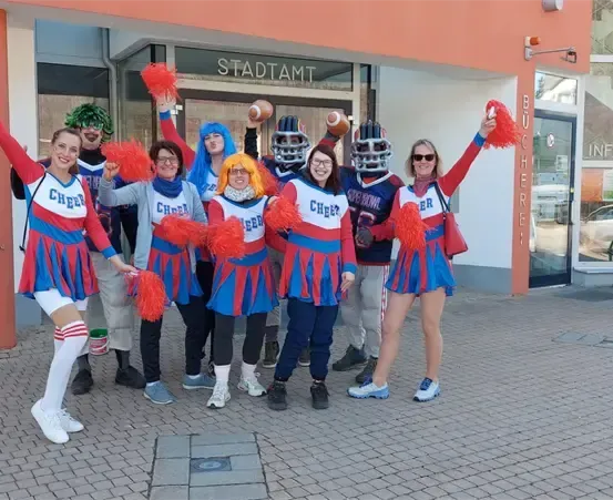 Eine Gruppe von Cheerleadern in blauen und roten Uniformen posiert für ein Foto vor einem Gebäude.