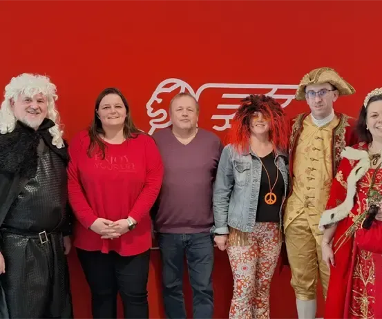 Eine Gruppe von Menschen in Kostümen posiert für ein Foto vor einer roten Wand.