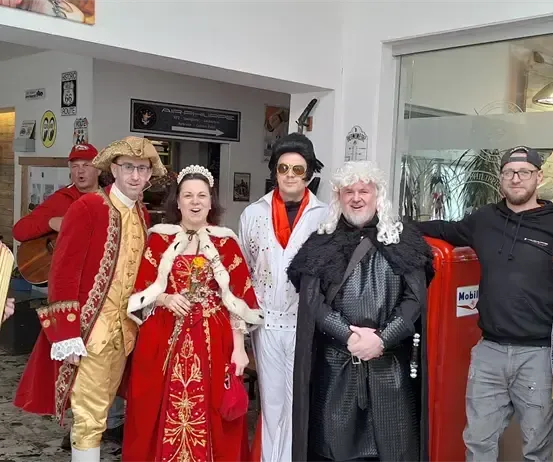 Eine Gruppe von Menschen in Kostümen posiert für ein Foto vor einem Gebäude. Einer spielt Akkordeon.