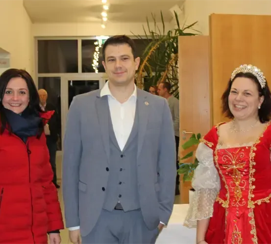 Eine Gruppe von Menschen in formeller Kleidung, eine Frau in einem roten Kleid, stehen zusammen in einem Raum.