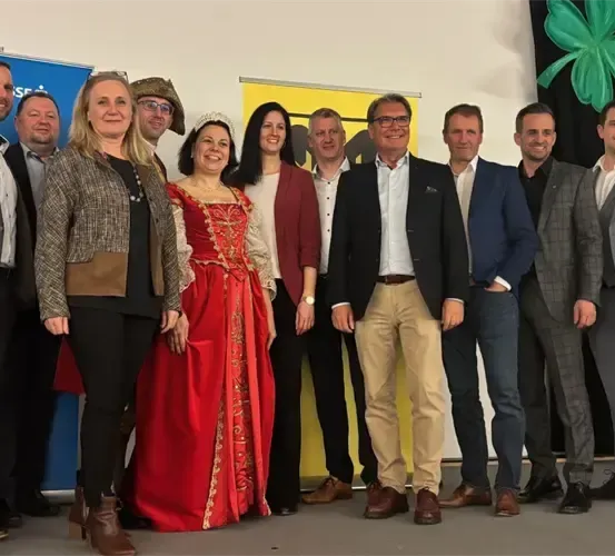 Eine Gruppe von Menschen in formeller Kleidung posiert für ein Foto vor einem blauen Banner und einem Kleeblatt-Design.