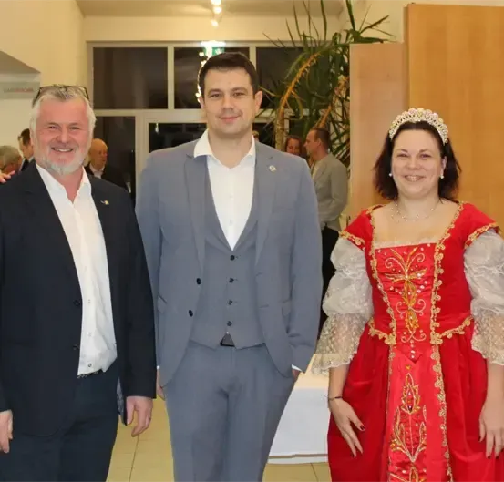 Eine Gruppe von Menschen in formeller Kleidung steht in einem Innenraum zusammen, mit einer Frau in einem roten Kleid und einem Mann in einem goldenen Kostüm.