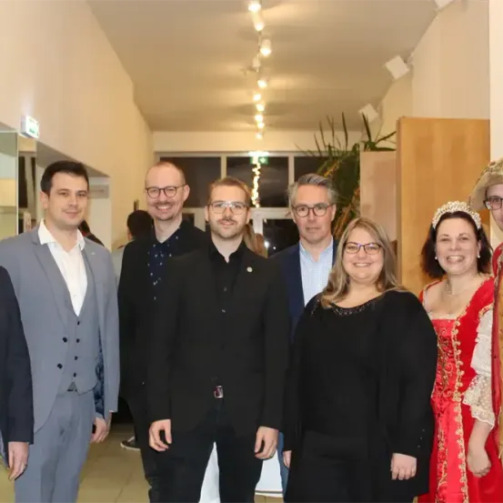 Eine Gruppe von Menschen posiert für ein Foto in einem Raum. Einige tragen formelle Kleidung, während andere Kostüme tragen.