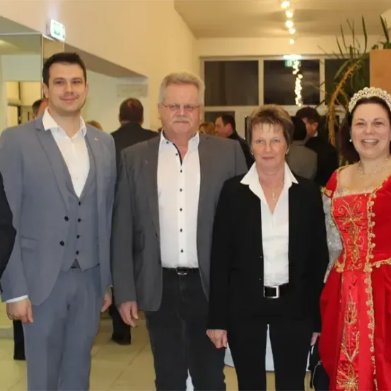 Fünf Menschen in formeller Kleidung posieren für ein Foto in einem Raum mit Glaswand und Pflanzen.