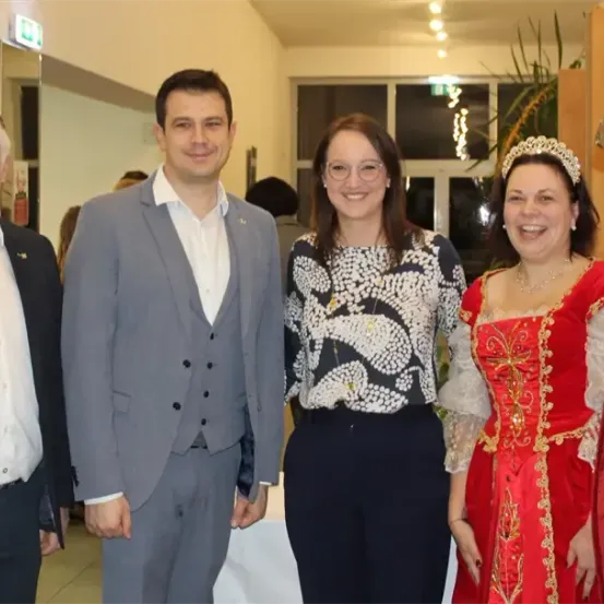 Fünf Menschen posieren für ein Foto in einem Saal. Ein Mann in Anzug und eine Frau in einem roten Kleid lächeln.