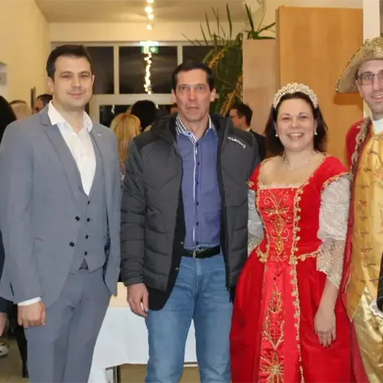 Eine Gruppe von Menschen in Kostümen und Anzügen posiert für ein Foto, lächelt und steht zusammen in einem Raum.