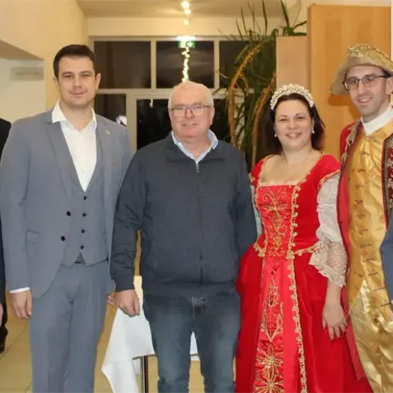 Eine Gruppe von Menschen posiert für ein Foto, darunter Männer in Anzügen und eine Frau in einem roten Kleid mit Krone.