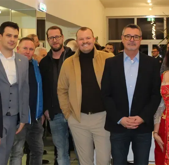 Eine Gruppe von Menschen steht in einem Raum mit einer festlichen Atmosphäre, wahrscheinlich bei einer Veranstaltung. Sie alle lächeln und scheinen für ein Foto zu posieren.