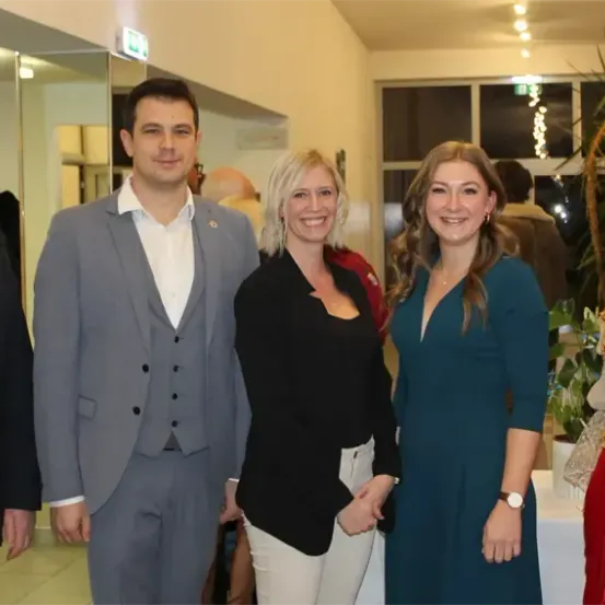 Eine Gruppe von fünf Personen, drei Männer und zwei Frauen, stehen zusammen in einem Raum. Sie lächeln und posieren für ein Foto.