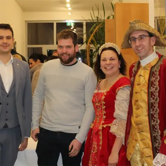 Vier Personen stehen zusammen und lächeln. Ein Mann in einem Kostüm und eine Frau in einem roten Kleid mit Krone.