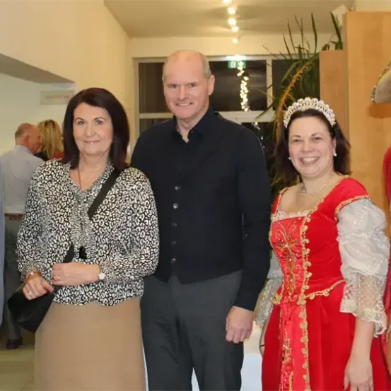 Eine Gruppe von Menschen in verschiedenen Kostümen, darunter eine Frau in einem roten Kleid und ein Mann in einem Piratenhut, posiert für ein Foto in einem Innenraum.